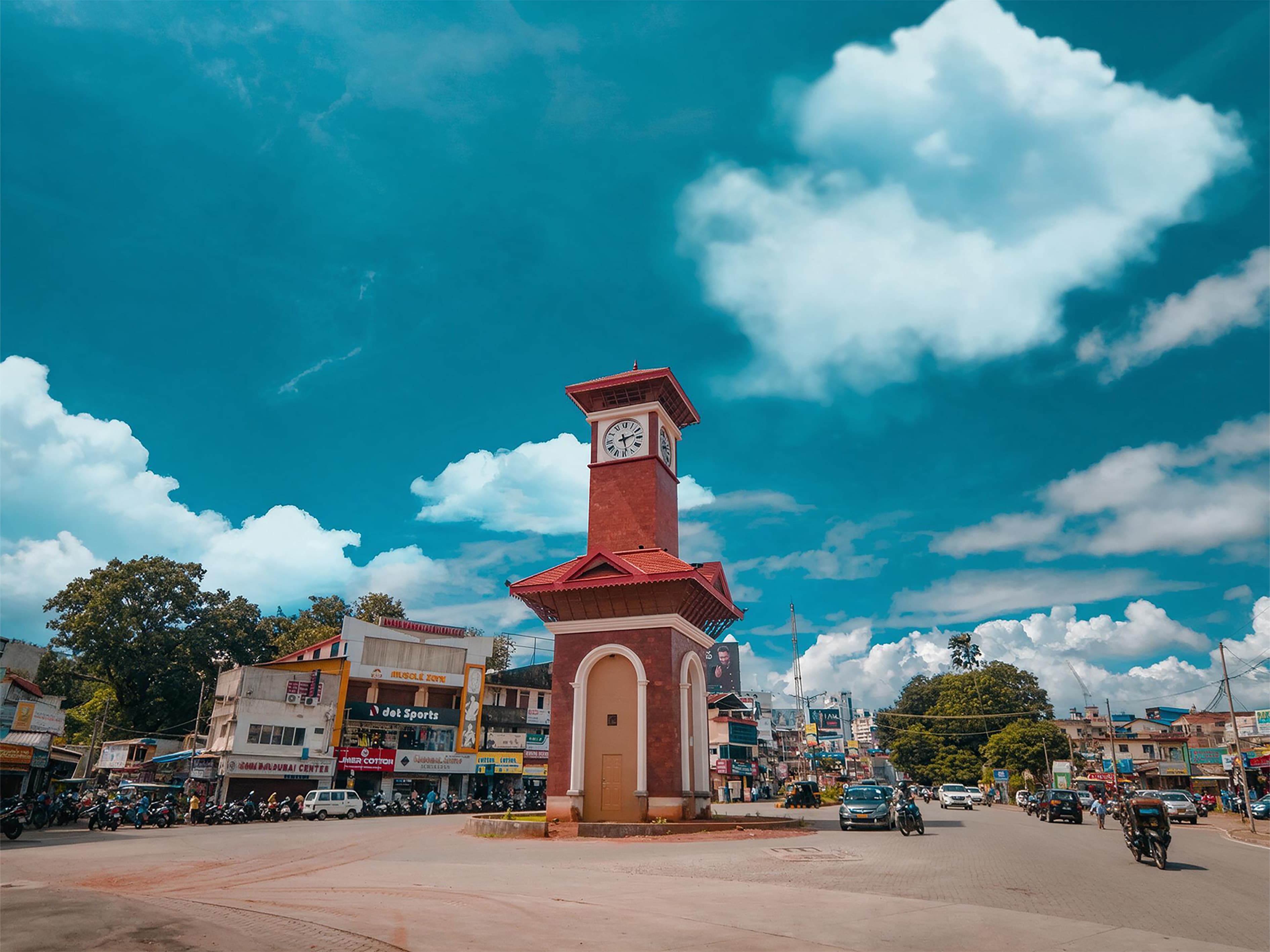 Red-brick clock tower at a busy town circle in Mangaluru under a bright blue sky